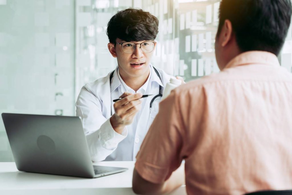 Confident doctor man holding a pill bottle while talking with a senior patient and reviewing his medication at office room.